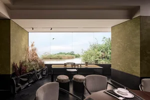 Modern restaurant interior with wooden table and chairs, overlooking a serene lake.