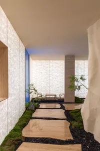 A minimalist courtyard with wooden stepping stones and a small table and chairs under a covered area.
