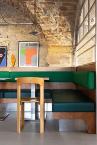 Modern restaurant interior featuring a contemporary seating area with wooden stools and upholstered booths, set against rusti