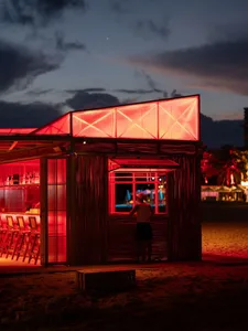 A beachside bar with bamboo walls and glass roof, featuring a person standing at the window.