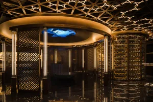 A wine bar featuring a circular metal mesh structure with illuminated shelves and a central island with a blue light feature.