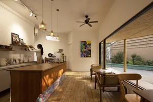 A minimalist cafe interior featuring a wooden counter and tables, with artwork on the walls and a view of the outdoor seating