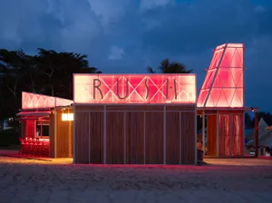 A minimalist modern beach bar with wooden and glass materials, illuminated by neon lights.