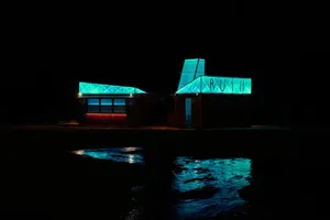 A modern restaurant exterior at night with a glass roof illuminated in blue light.