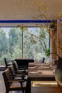 A modern restaurant interior with sleek, minimalist design and large windows showcasing a green outdoor environment.