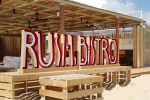 Wooden beach bar with large 'RUSH BISTRO' sign in red letters.