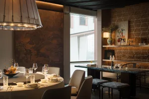 A contemporary restaurant interior with metallic walls, carpeted flooring, and stone tables.