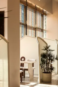 A modern restaurant interior featuring a neutral-toned color palette, natural lighting through tall windows, and a cozy seati