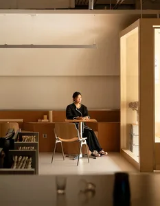 A person sitting alone at a table in a cafe with wooden furniture and minimalist design.