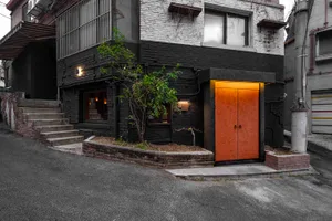 A black brick building with an orange door and a small green tree in front of it.