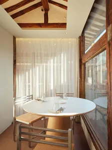 A minimalist dining room with a round table, chairs, and sheer white curtains.