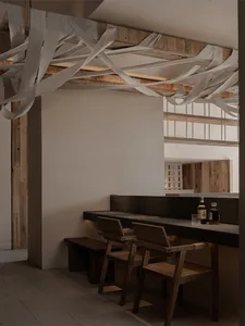 A minimalist restaurant interior featuring a bar counter with a concrete surface and wooden chairs.