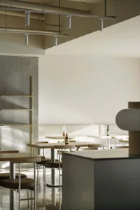 A modern restaurant interior featuring minimalist design, wooden tables, and concrete finishes.