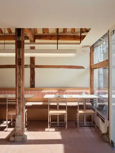 Modern minimalist restaurant interior with wooden seating, metal tables, and terracotta floor tiles.