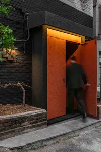 A person entering a building through a large, wide, red-brick entrance with illuminated light within.