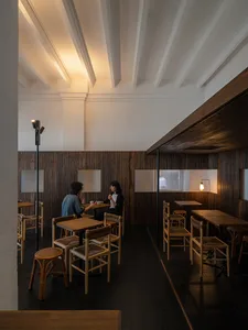 People enjoying drinks in a minimalist cafe interior with wooden furniture and walls.