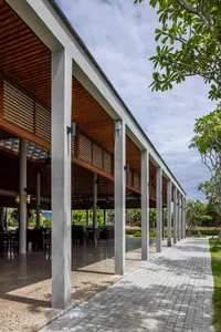 Modern bar area with concrete pillars, timber ceiling, and glass walls overlooking a green courtyard.