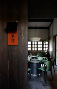A modern restaurant interior featuring wooden materials and a round dining table with green chairs.