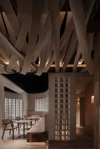 A minimalist restaurant interior featuring wooden tables, chairs, and ceiling beams.