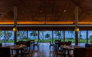 A modern restaurant interior with wooden ceiling and glass walls overlooking the coast.