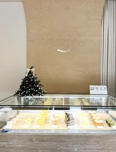 A glass bakery display case featuring various slices of cakes and desserts, adorned with a small, decorated Christmas tree.