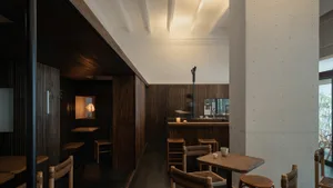 A minimalist restaurant interior featuring dark wood paneling and wooden furniture.