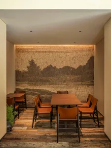 A modern restaurant interior featuring wooden tables and chairs with leather upholstery, a scenic mural on the wall depicting
