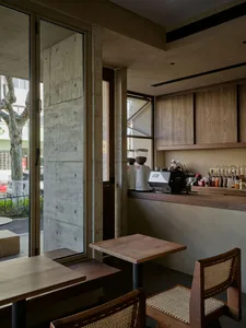 A modern cafe interior with wooden tables and chairs, featuring minimalist design elements and exposed concrete columns.