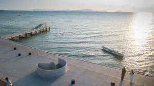 A concrete pier extends into the water with a boat nearby and mountains in the distance.