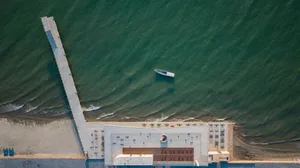 Aerial view of a modern beachfront architectural design featuring a concrete structure with a pier extending into the water.