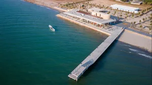 A modern, concrete restaurant building adjacent to a beach with a long jetty extending into the sea.