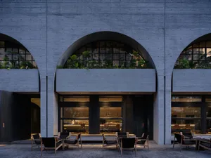 Modern restaurant with concrete exterior, glass accents, and greenery.