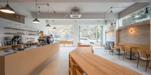 Modern coffee shop interior with wooden tables and chairs, large windows, and a minimalist design.