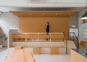 A modern coffee shop interior featuring a wooden design with a stage-like raised seating area and minimalist decor.