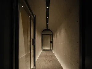 A minimalist corridor with concrete walls and a tiled floor, featuring a single door at the end.