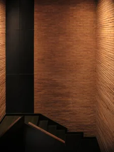 Modern industrial staircase with brick walls, black flooring, and wooden handrails.