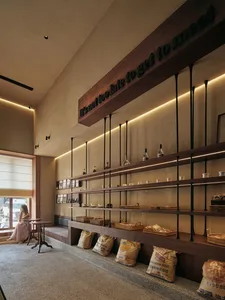 A cozy coffee shop with concrete shelves displaying various items and a woman sitting at a small table.