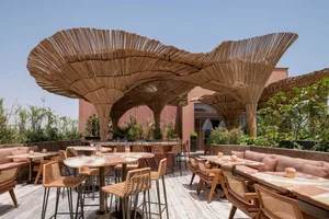An outdoor cafe with modern furniture and a unique, natural wooden canopy