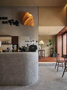 A modern coffee shop featuring concrete and terrazzo materials with a croissant-shaped light fixture and a counter bar.