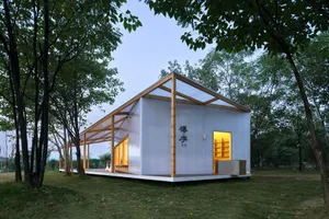 Modern residential house with metallic panels and glass roof, set in a green landscape.