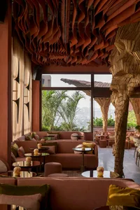 Indoor seating area of a modern restaurant with fabric sofas, wooden elements, and large windows overlooking greenery.