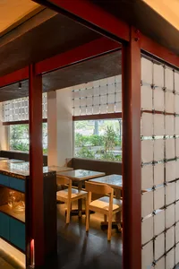 Interior view of a modern restaurant with wooden tables, concrete walls, and glass dividers.
