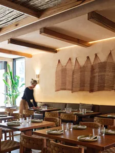 A modern restaurant interior featuring wooden tables, chairs, and decorative wall hangings.