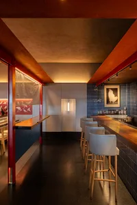 A modern restaurant interior featuring a wooden bar counter and concrete wall tiles.