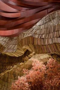 An overhead view of a wooden structure composed of numerous thin, vertical wooden sticks arranged in a wave-like pattern.
