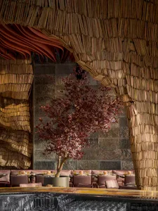 A restaurant interior with wooden decor and red-leafed tree in the center.