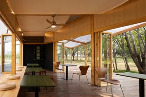 Modern cafe interior with wooden furniture, ceiling fan, and hanging light fixture.