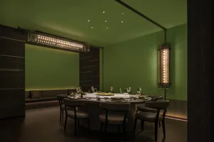 A modern restaurant dining room with dark green walls and illuminated lighting.