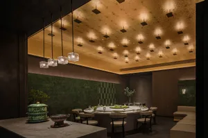A modern restaurant with marble and concrete walls, featuring a large dining table and pendant lights.