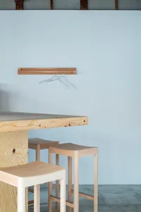 Minimalist interior design featuring wooden stools and a wooden table against a white wall with a wooden hanger.